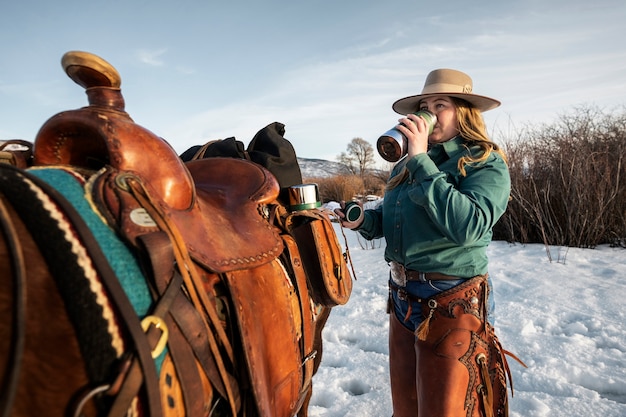 Ritratto di cowgirl che beve accanto a un cavallo