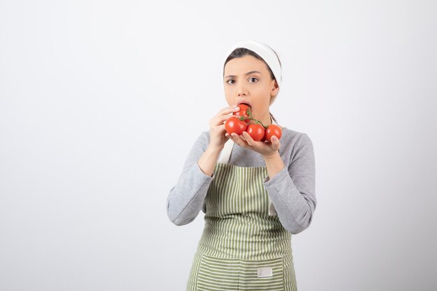 Ritratto di donna affamata che mangia pomodori rossi sul muro bianco