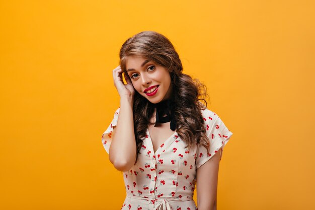 Ritratto di donna affascinante in abito bianco. Bella ragazza giovane con rossetto luminoso in abiti stampa ciliegia che esamina la macchina fotografica.