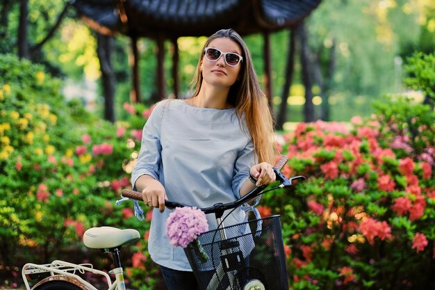 Ritratto di donna attraente con bicicletta da città vicino al padiglione cinese tradizionale in un parco.