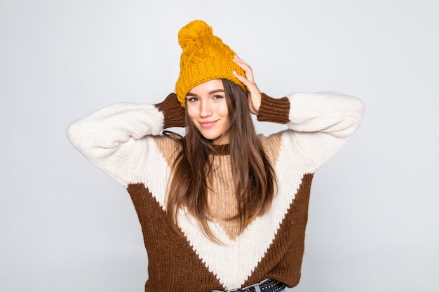 Ritratto di donna bella inverno. Ragazza sorridente che porta i vestiti caldi divertendosi cappello e maglione isolati sulla parete bianca