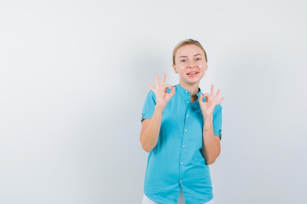 Ritratto di donna bionda che mostra gesto ok in camicetta blu e sembra felice vista frontale