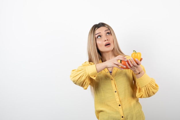 Ritratto di donna bionda che tiene i peperoni dolci colorati sul muro bianco.