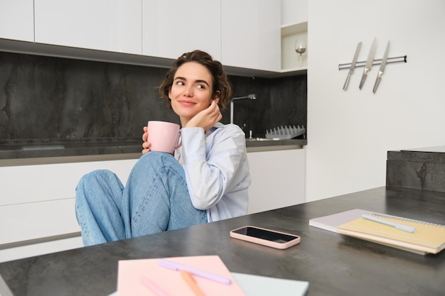 Ritratto di donna bruna sorridente siede a casa beve una tazza di tè in cucina si rilassa e gode di un giorno libero