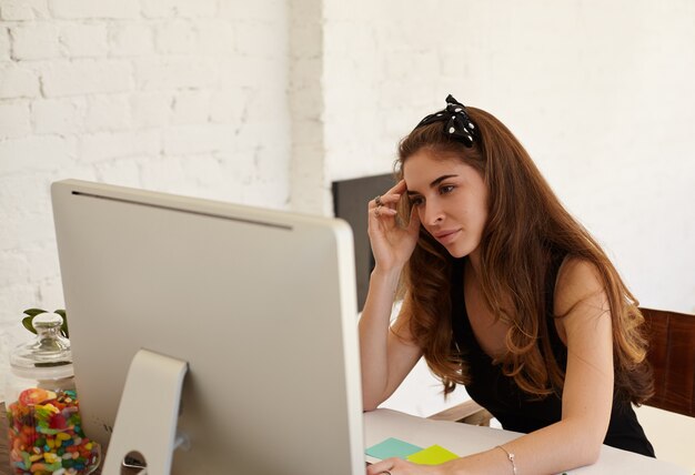 Ritratto di donna caucasica economista sta analizzando le attività dell'azienda tramite PC seduto davanti al computer in ufficio. Giovane imprenditrice che lavora sodo per raggiungere gli obiettivi aziendali