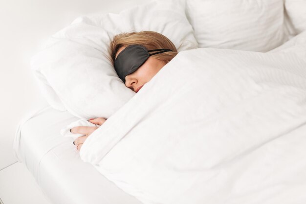 Ritratto di donna che indossa una maschera per gli occhi neri mentre dorme a letto a casa