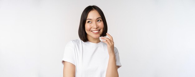 Ritratto di donna civettuola carina ridere e sorridere guardando da parte pensiero premuroso o imaging smth in piedi in maglietta bianca su sfondo per studio