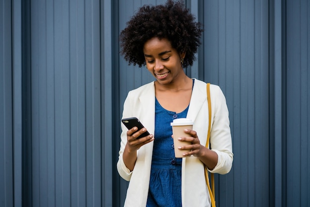 Ritratto di donna d'affari afro che usa il suo telefono cellulare mentre si trova all'aperto in strada