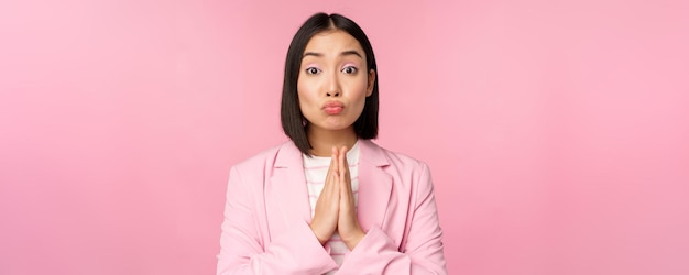 Ritratto di donna d'affari asiatica che chiede aiuto dire per favore in piedi in preghiera implorando posa rosa stu