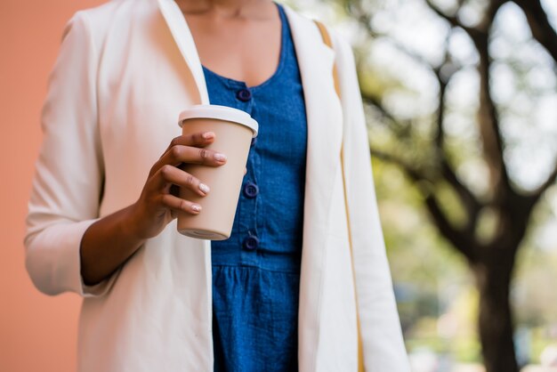Ritratto di donna d'affari che tiene una tazza di caffè mentre levandosi in piedi all'aperto sulla strada. Business e concetto urbano.