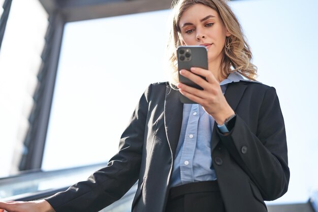 Ritratto di donna d'affari in tuta in piedi sulla scala mobile a piedi in città utilizzando il telefono cellulare aziendale
