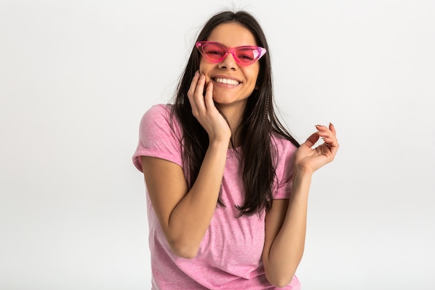 Ritratto di donna emotiva abbastanza sorridente in camicia rosa e occhiali da sole alla moda, denti bianchi, posa positiva isolata
