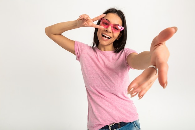 Ritratto di donna emotiva abbastanza sorridente in camicia rosa e occhiali da sole tenendo le braccia in avanti