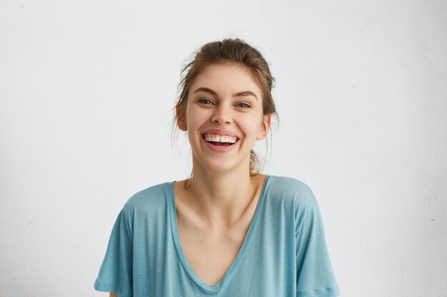 Ritratto di donna felice che sorride sinceramente. Donna europea con un ampio sorriso in camicetta casual blu in posa contro il muro bianco