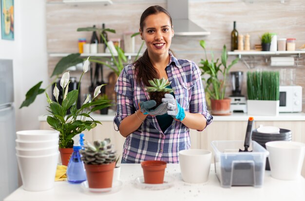 Ritratto di donna felice che tiene una pianta succulenta seduta sul tavolo in cucina