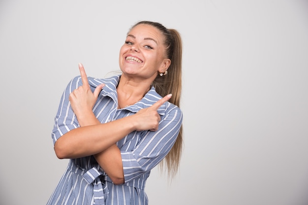 Ritratto di donna graziosa che indica qualcosa sul muro grigio.