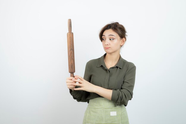 Ritratto di donna graziosa in grembiule che tiene un mattarello. Foto di alta qualità