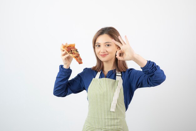 Ritratto di donna in grembiule che mostra una fetta di pizza su bianco