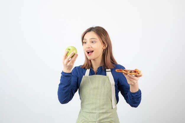 Ritratto di donna in grembiule che sceglie mela da mangiare sopra la pizza