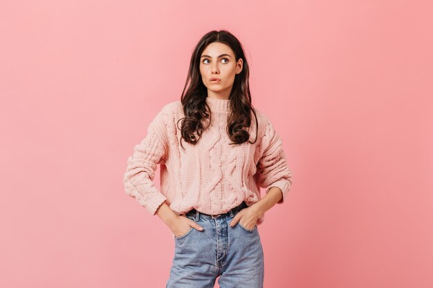 Ritratto di donna in maglione lavorato a maglia e blue jeans su sfondo isolato. Bella ragazza carina si morde il labbro.