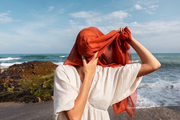 Ritratto di donna in spiaggia che copre il viso con il velo