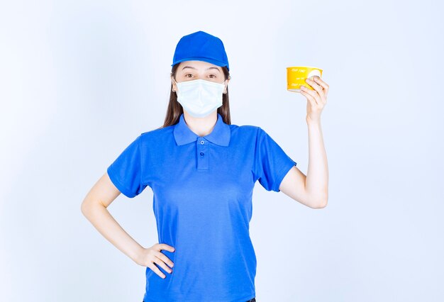 Ritratto di donna in uniforme e maschera medica che tiene tazza di plastica