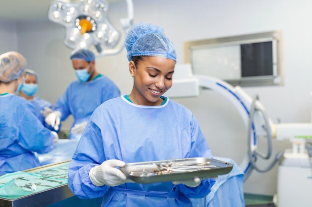 Ritratto di donna infermiere chirurgo O membro del personale vestito con scrub chirurgico camice maschera e retina per capelli nel teatro della sala operatoria dell'ospedale rendendo il contatto visivo sorridente contento felice guardando la fotocamera