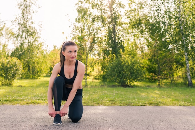 Ritratto di donna jogging attiva che riposa e prepara le scarpe per l'allenamento nel parco