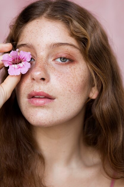 Ritratto di donna lentigginosa che copre l'occhio con un fiore