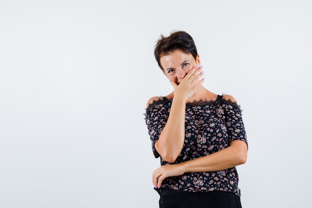 Ritratto di donna matura che copre la bocca con la mano in camicetta e guardando felice vista frontale