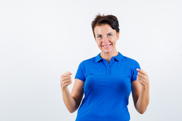 Ritratto di donna matura che mostra il gesto del vincitore in maglietta blu e guardando felice vista frontale