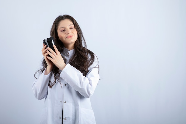 Ritratto di donna medico con una tazza di caffè che dorme sul muro bianco.