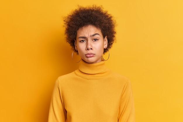 Ritratto di donna millenaria scontenta con i capelli afro aggrotta le sopracciglia si sente infelice ha alcuni problemi vestito con dolcevita casual.