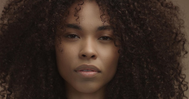 Ritratto di donna nera di razza mista con grandi capelli ricci afro su sfondo beige Primo piano del viso con pelle ideale Trucco naturale