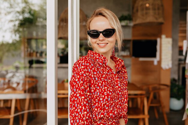 Ritratto di donna piuttosto affascinante con i capelli biondi con gli occhiali e vestito luminoso e sorridente