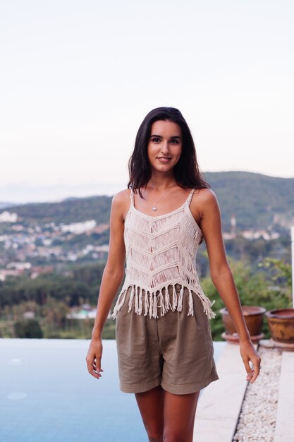 Ritratto di donna romantica calma caucasica felice in look casual con capelli lunghi che indossa orecchini e collana su sfondo incredibile bella vista sulle montagne verdi