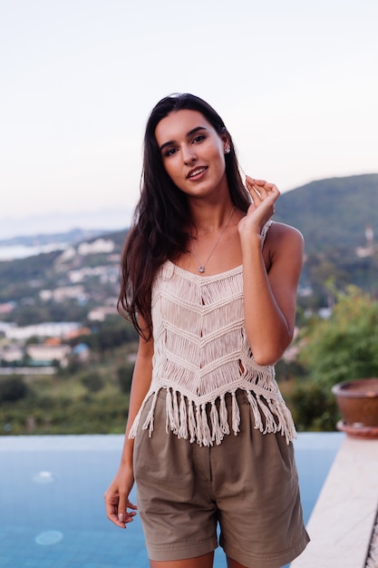 Ritratto di donna romantica calma caucasica felice in look casual con capelli lunghi che indossa orecchini e collana su sfondo incredibile bella vista sulle montagne verdi