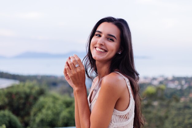 Ritratto di donna romantica calma caucasica felice in look casual con capelli lunghi che indossa orecchini e collana su sfondo incredibile bella vista sulle montagne verdi