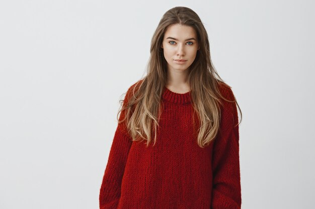 Ritratto di donna sensuale attraente giovane 25s in maglione accogliente rosso seduto a casa confortevole, godendo guardando la neve che cade per le strade, guardando in posa contro