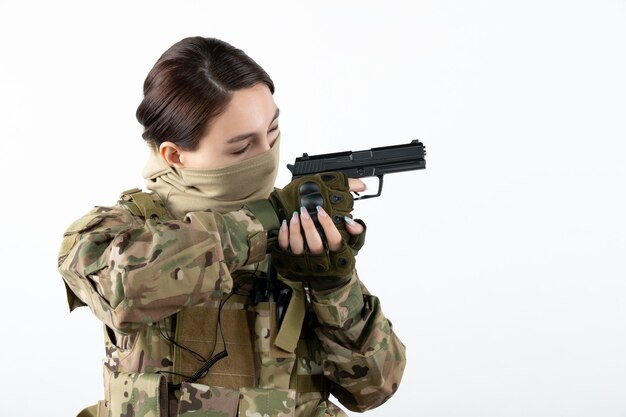 Ritratto di donna soldato con pistola in mimetica parete bianca