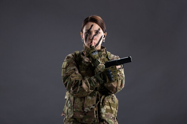 Ritratto di donna soldato con pistola in mimetica parete scura