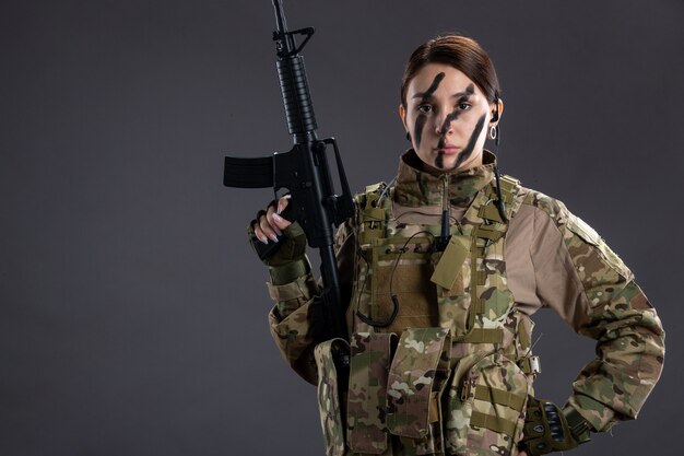 Ritratto di donna soldato in uniforme militare con mitragliatrice sul muro scuro