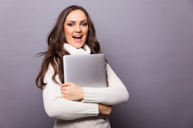 Ritratto di donna sorpresa felice in piedi con il computer portatile isolato sul muro grigio