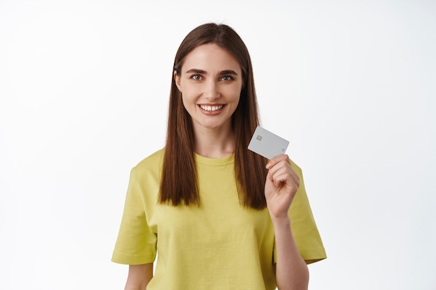 Ritratto di donna sorridente che paga con carta di credito, pubblicità di pagamento contactless, trasferimento di denaro o sistema di cashback, in piedi su sfondo bianco. Acquisti online.