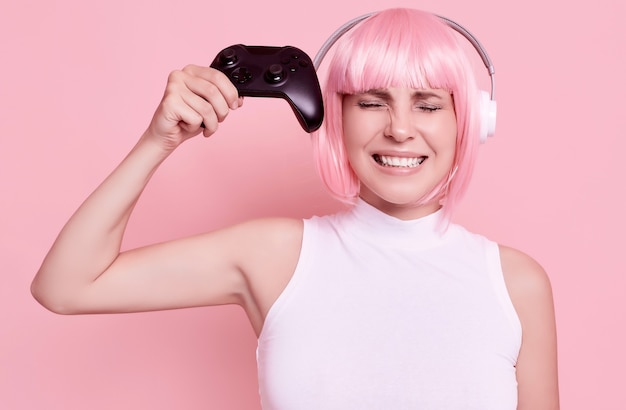 Ritratto di donna splendida con capelli rosa, giocare ai videogiochi utilizzando il joystick in studio