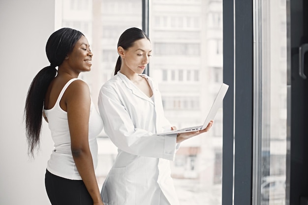 Ritratto di dottoressa caucasica e paziente nero in piedi in ufficio in clinica