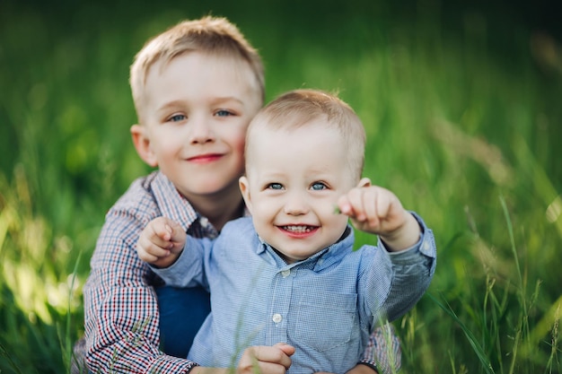 Ritratto di due fratellini felici alla moda con bellissimi occhi azzurri che giocano nel parco abbracciando e guardando la telecamera Ragazzi che indossano magliette in posa su sfondo verde erba