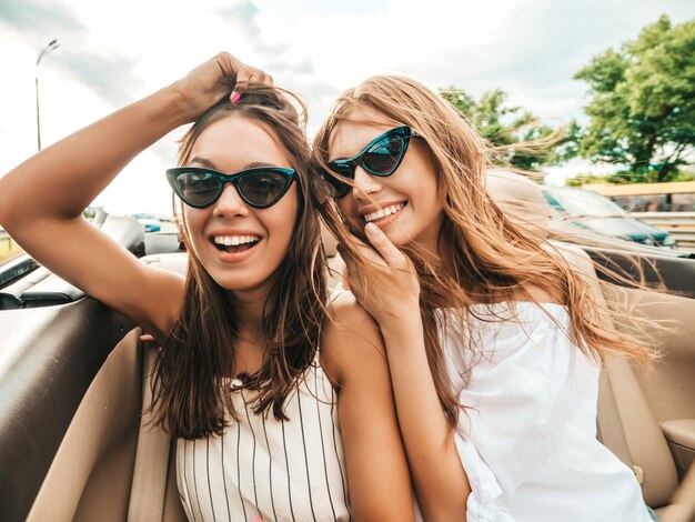 Ritratto di due giovani belle e sorridenti donne hipster in auto decappottabile