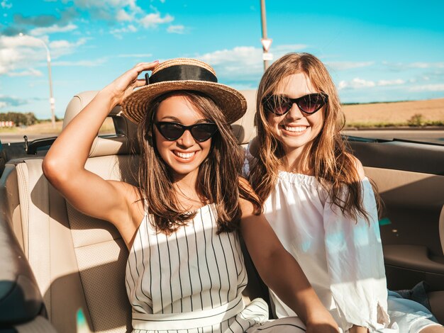 Ritratto di due giovani belle e sorridenti donne hipster in auto decappottabile