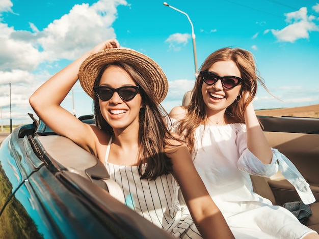 Ritratto di due giovani belle e sorridenti donne hipster in auto decappottabile